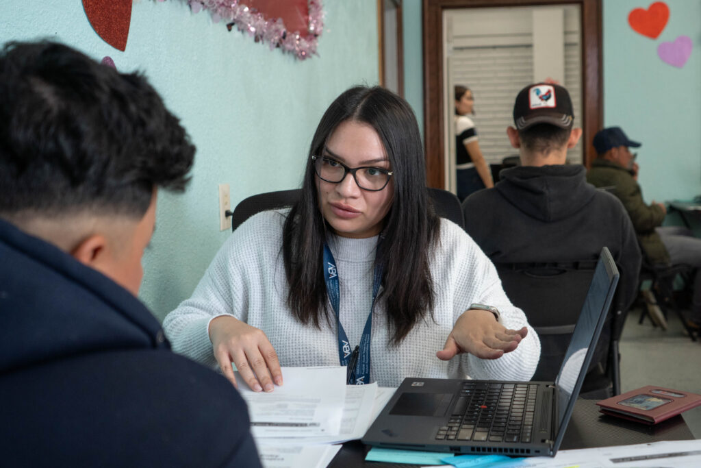 A ProBAR team member wearing a white sweater, long black hair, and glasses assists a young man with filling out a Work Authorization form. 